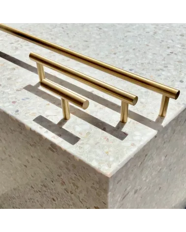 Brass T-Bar cabinet knob design handle side view on a stone surface with handles aligned in the background