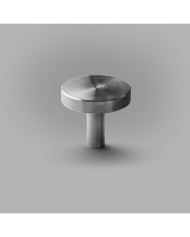 Polished chrome NENA M furniture knob, designer handle placed on a grey surface