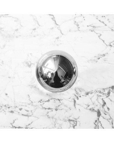 Polished chrome ODETE M furniture knob, designer handle placed on a marble surface